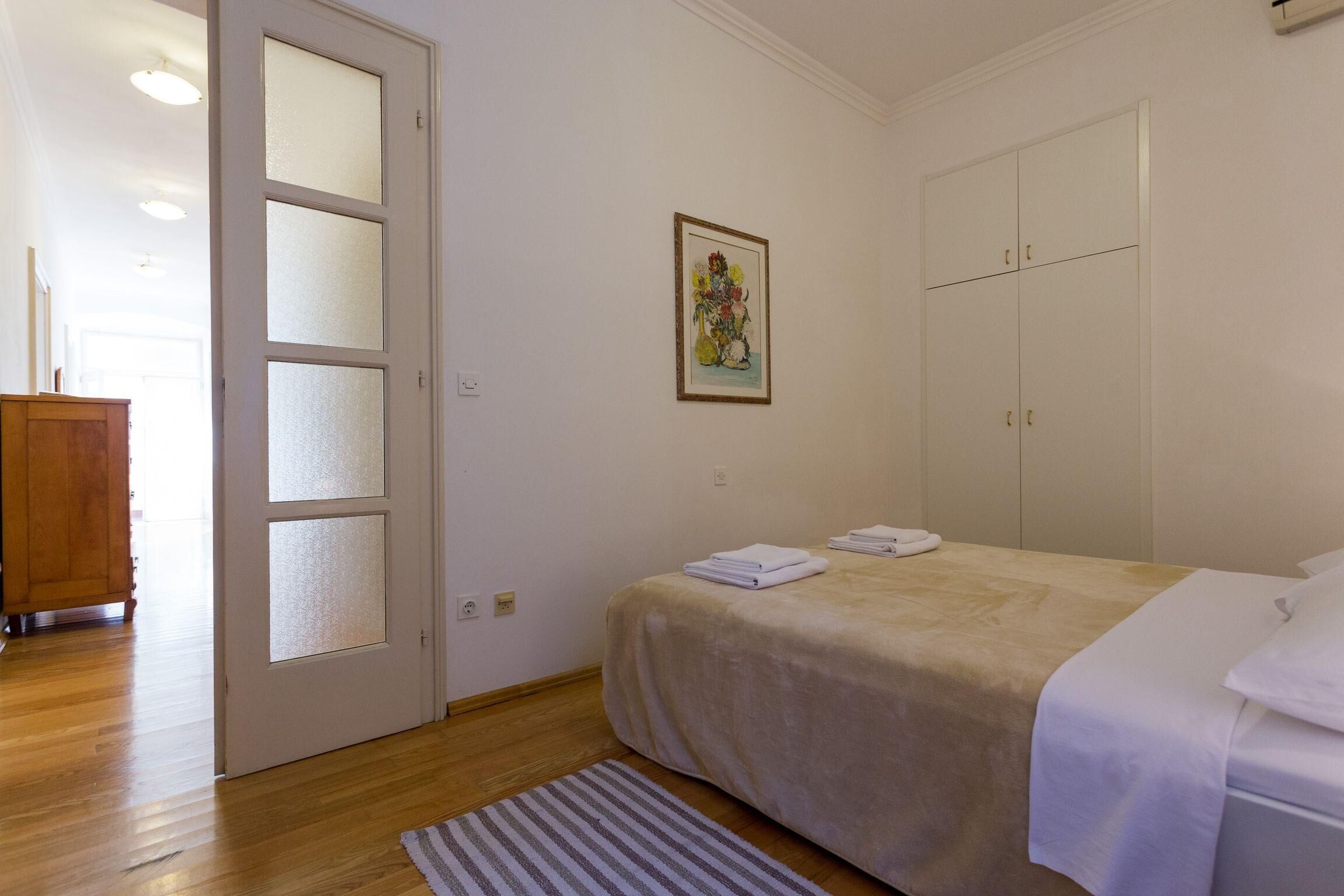 A bedroom with a bed, a wardrobe, a door, and a painting on the wall.