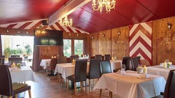 A restaurant with wooden paneling, chandeliers, and tables set with candles and glassware.