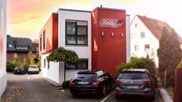A narrow street with two parked cars and a building with a red facade and a sign that reads "Schlafgug."