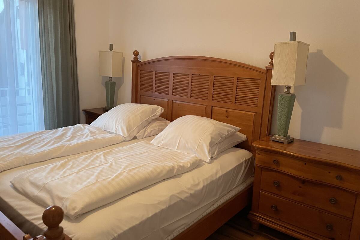 Una cama doble con cabecera de madera y dos mesitas de noche con lámparas.