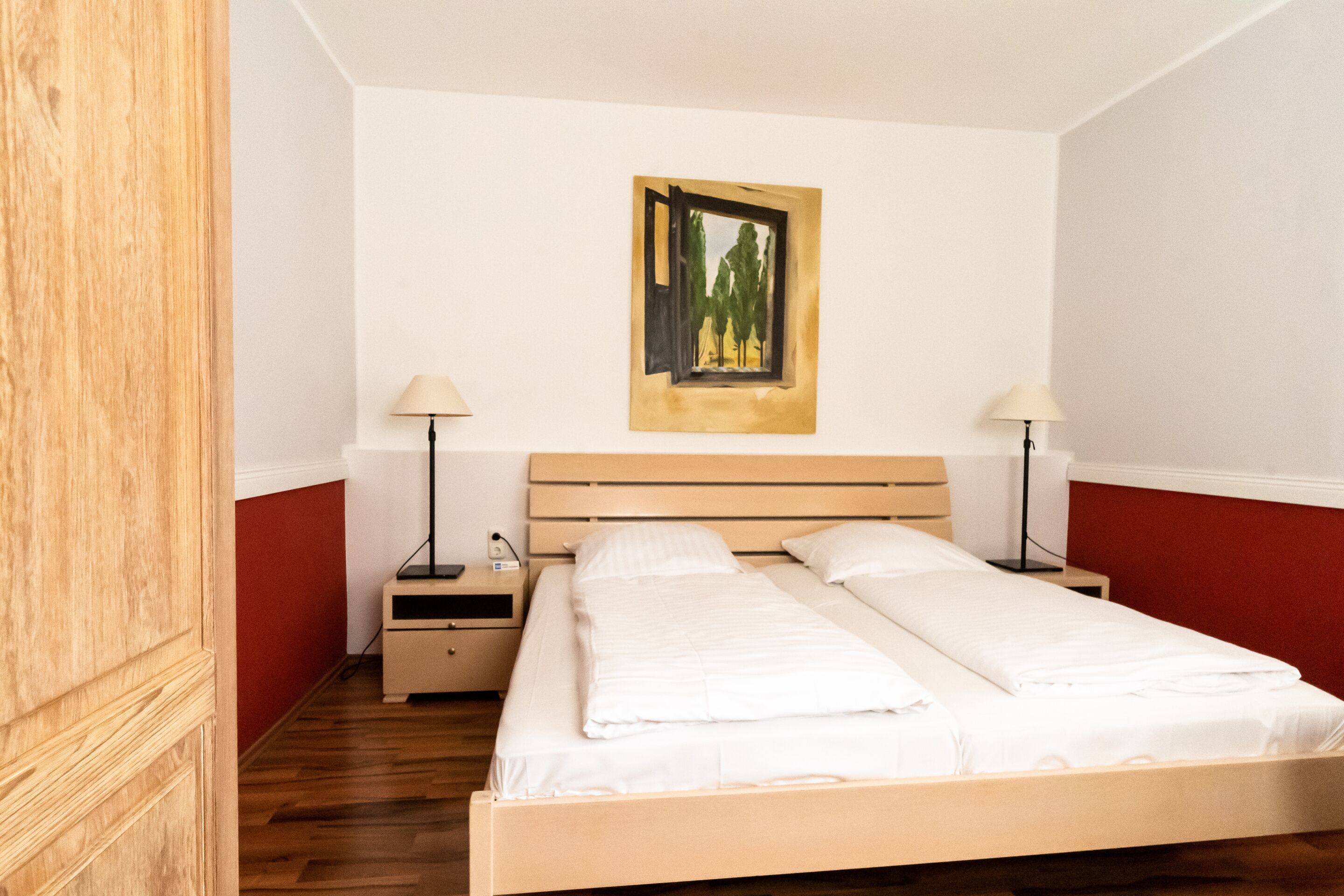 A bedroom with a wooden bed, white bedding, two bedside tables with lamps, and a painting on the wall.