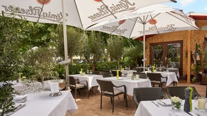 Een terras met tafels gedekt voor gasten, omringd door groen en stenen muren.