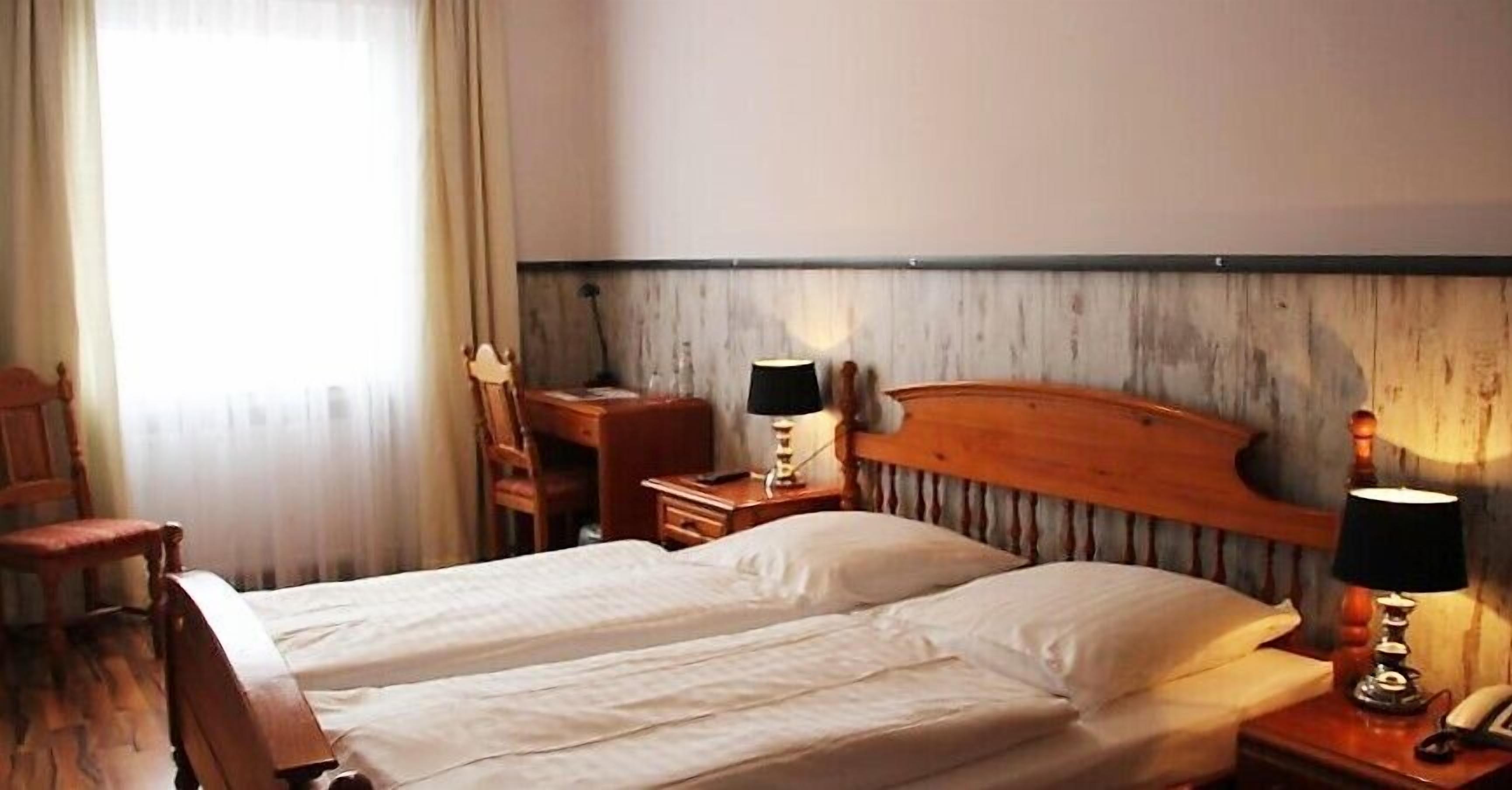 Habitación de hotel con dos camas individuales, cabecero de madera, escritorio con silla y dos lámparas de noche.
