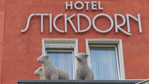 Een hotelschilder met de naam 'STICKDORN' en twee stenen schapenbeeldjes op het balkon.