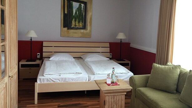 Une chambre d’hôtel avec un lit, deux tables de chevet, un canapé vert, un tableau au mur et un plancher en bois.