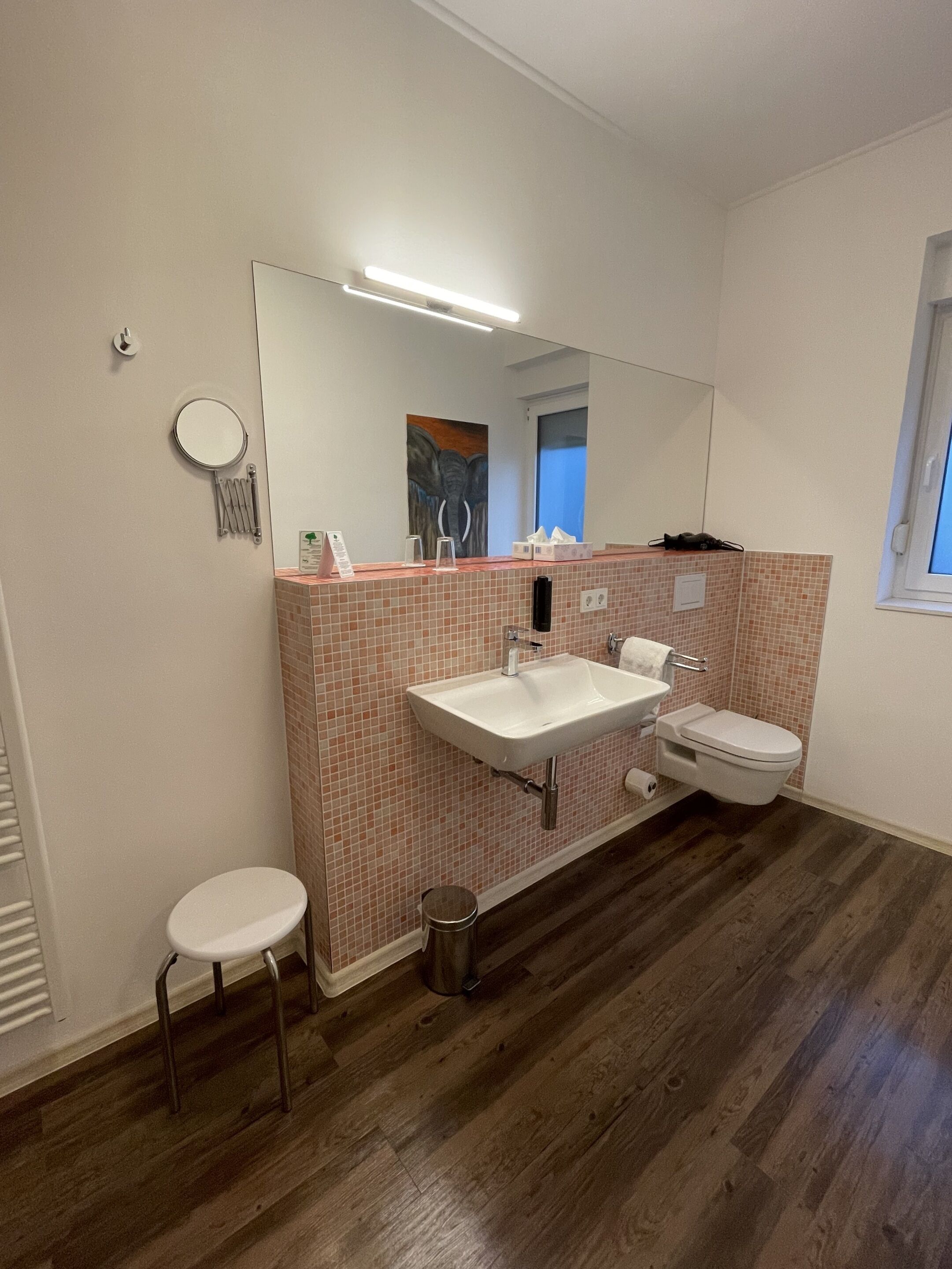 A bathroom with a white sink, a toilet, a mirror, and a small stool.
