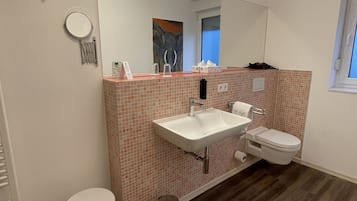 A bathroom with a white sink, a toilet, a mirror, and a small stool.
