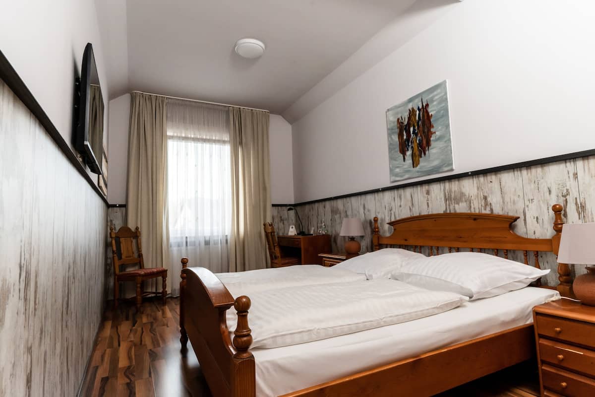 Habitación de hotel con una cama de madera, un escritorio, una silla, un televisor y un cuadro en la pared.