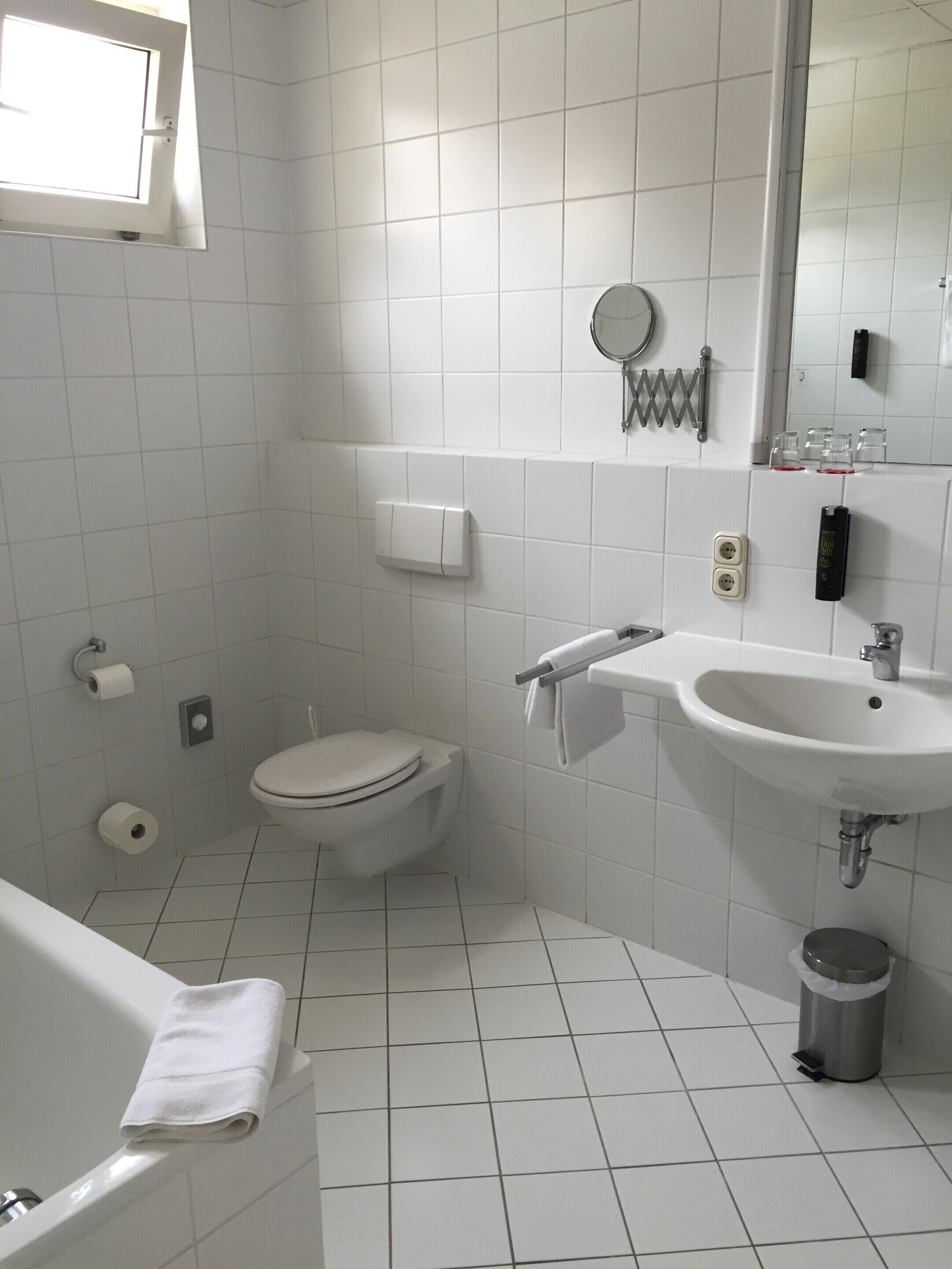 Ein kleines Badezimmer mit weißen Fliesen, einer Toilette, einem Waschbecken und einer Badewanne.