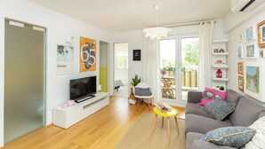 A modern living room with a flat-screen TV, a sofa, a small table, and a chair. There is a sliding glass door leading to an outdoor area. - Hedera Estate, Hedera A29 (Dubrovnik)