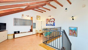 Un vaste espace de vie doté d’un haut plafond, de poutres apparentes, d’un escalier avec une rampe en métal, d’un téléviseur à écran plat, d’une table à manger et d’un canapé.