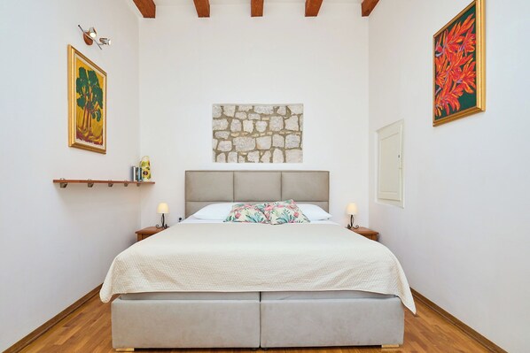 A bedroom with a bed, a stone wall, and two paintings.