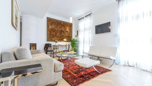 Un salon moderne avec un canapé, un pouf, une table basse en verre et un tapis rouge à motifs.
