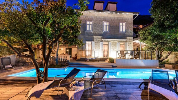 Un espace aménagé au bord de la piscine, avec des chaises longues et un bâtiment en pierre en arrière-plan.
