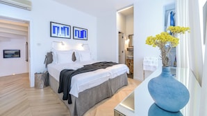 Une chambre à coucher moderne avec un lit, des lampes de chevet, un grand vase rempli de fleurs et une vue sur la salle de bain.