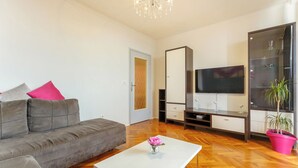 A modern living room with a grey sofa, a white coffee table with a vase, a TV, and a large cabinet with glass doors.