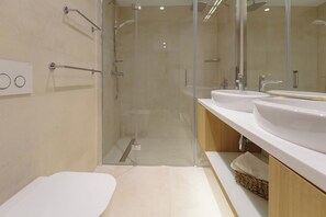 Une salle de bain moderne avec une douche à parois de verre, deux lavabos et des toilettes.