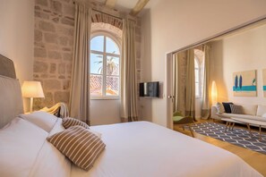 Habitación de hotel con una cama grande, televisión, sofá y vistas a palmeras a través de una ventana.