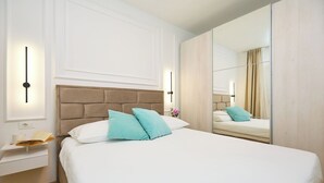 Une chambre d’hôtel avec un grand lit, une table de chevet avec une lampe, un miroir et un plancher en bois.