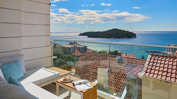 Un balcon avec vue sur la mer, un toit en tuiles et une table en bois avec un verre de vin.