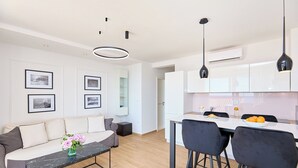 Une cuisine moderne avec des meubles blancs, un coin repas avec des chaises noires et un salon avec un canapé et une table basse.