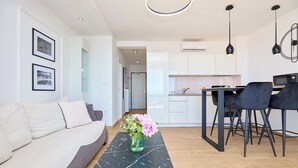 Un salon moderne avec un canapé, une table basse ornée d’un vase de fleurs, un coin repas avec des chaises, et une cuisine en arrière-plan.