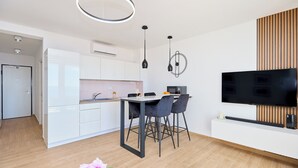 Une cuisine moderne avec des meubles blancs, une table à manger avec des chaises, un téléviseur à écran plat fixé au mur et des luminaires suspendus.