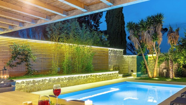 Zona de piscina con mesa de madera, dos copas de vino tinto y velas.