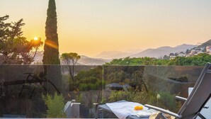 Un balcón con una mesa, una silla y vistas a un paisaje montañoso al atardecer.