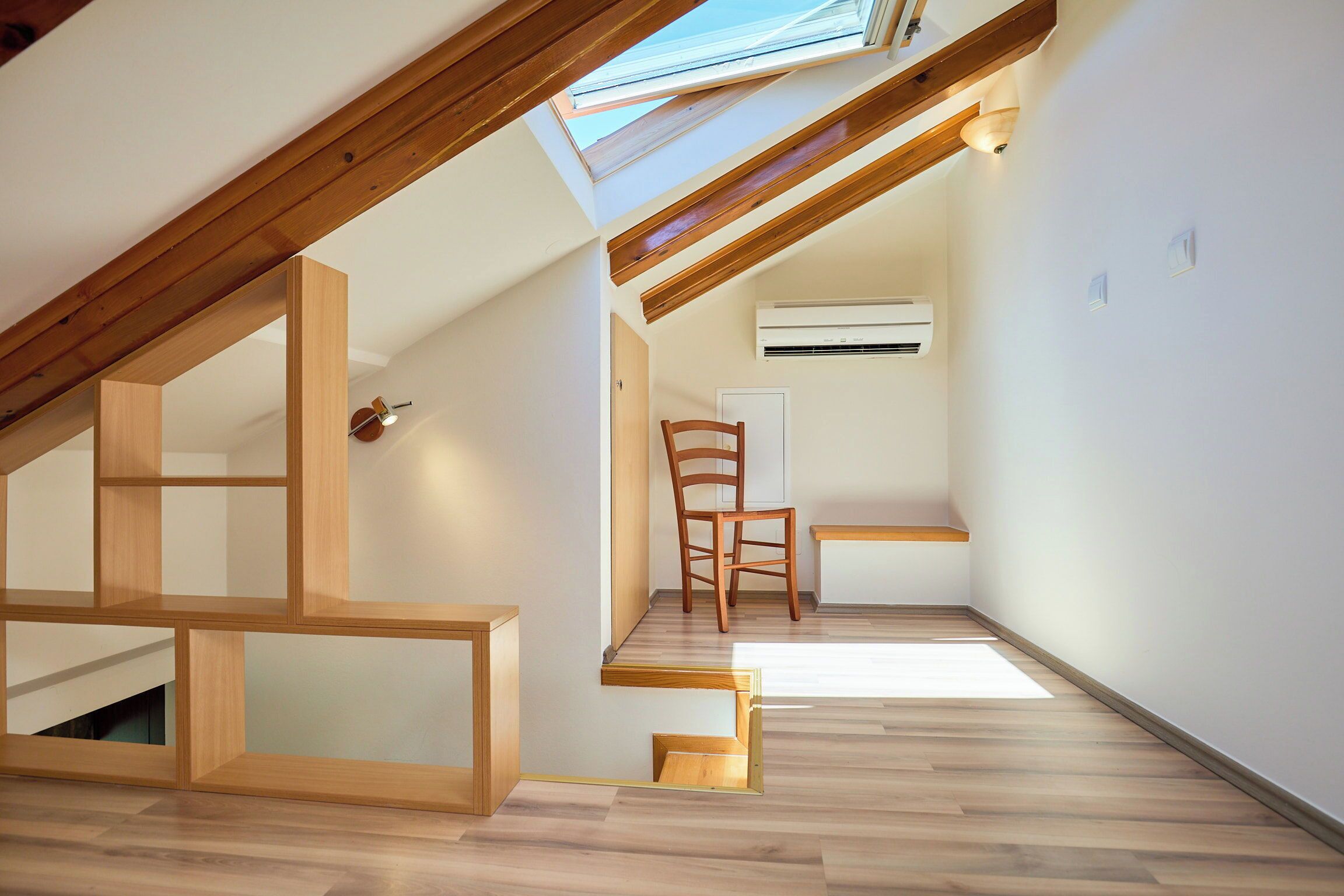 Un interior moderno con tragaluces, vigas de madera, una silla y una pared blanca con un equipo de aire acondicionado.
