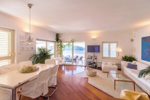 Un salon moderne comprenant un coin repas, des meubles blancs, une grande fenĂȘtre et une vue sur lâextĂ©rieur.