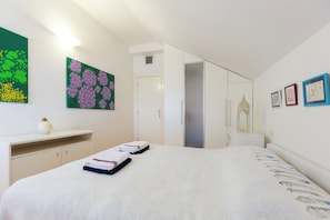 Une chambre à coucher comprenant un lit, un bureau, une armoire et une porte donnant sur une autre pièce.