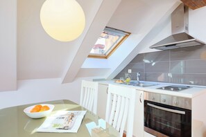 A modern kitchen with a skylight, white cabinetry, a built-in oven, and a glass dining table with a bowl of fruit. - Hedera Estate, Hedera A31 - Breakfast included (Dubrovnik)