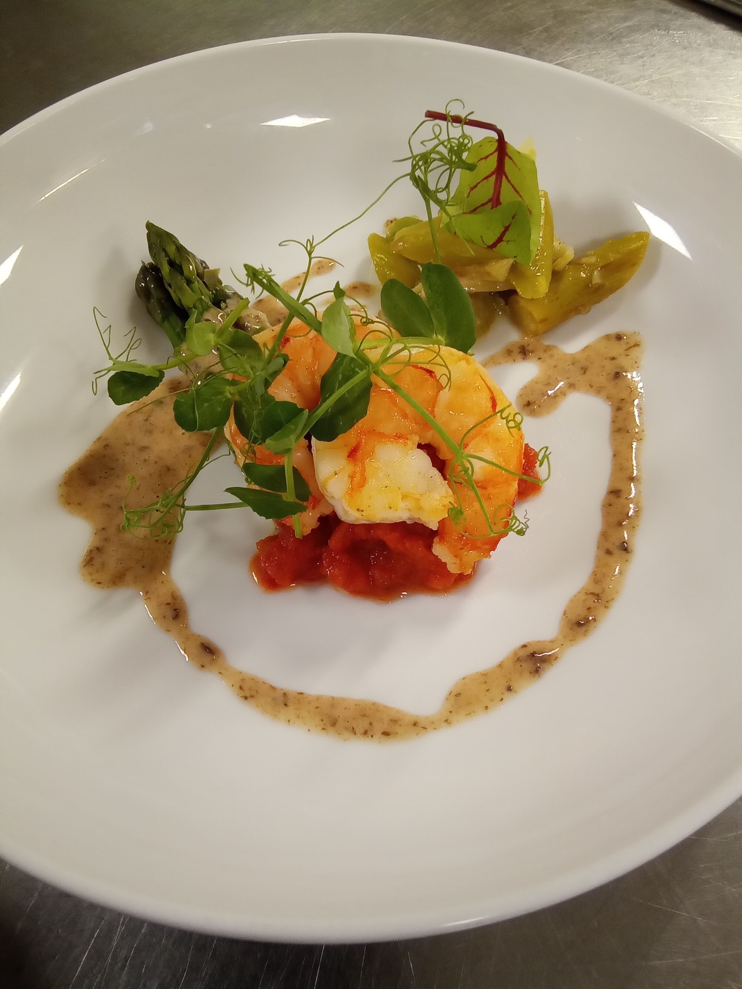 A white plate with a seafood dish, possibly lobster, garnished with greens and a sauce.