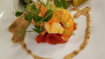 A white plate with a seafood dish, possibly lobster, garnished with greens and a sauce.