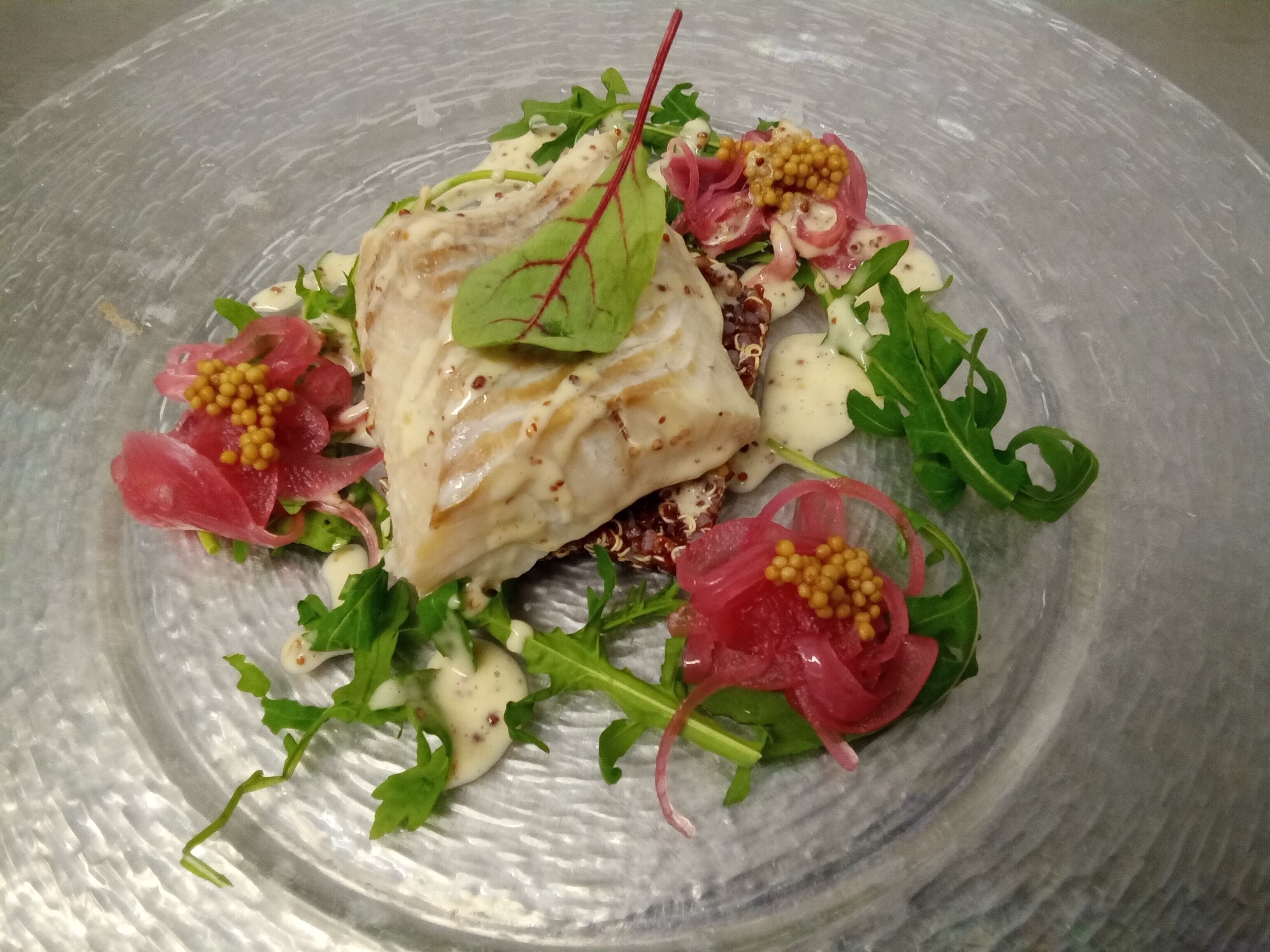 Ein Teller mit Fisch, Grünzeug und einer roten Blattgarnitur.