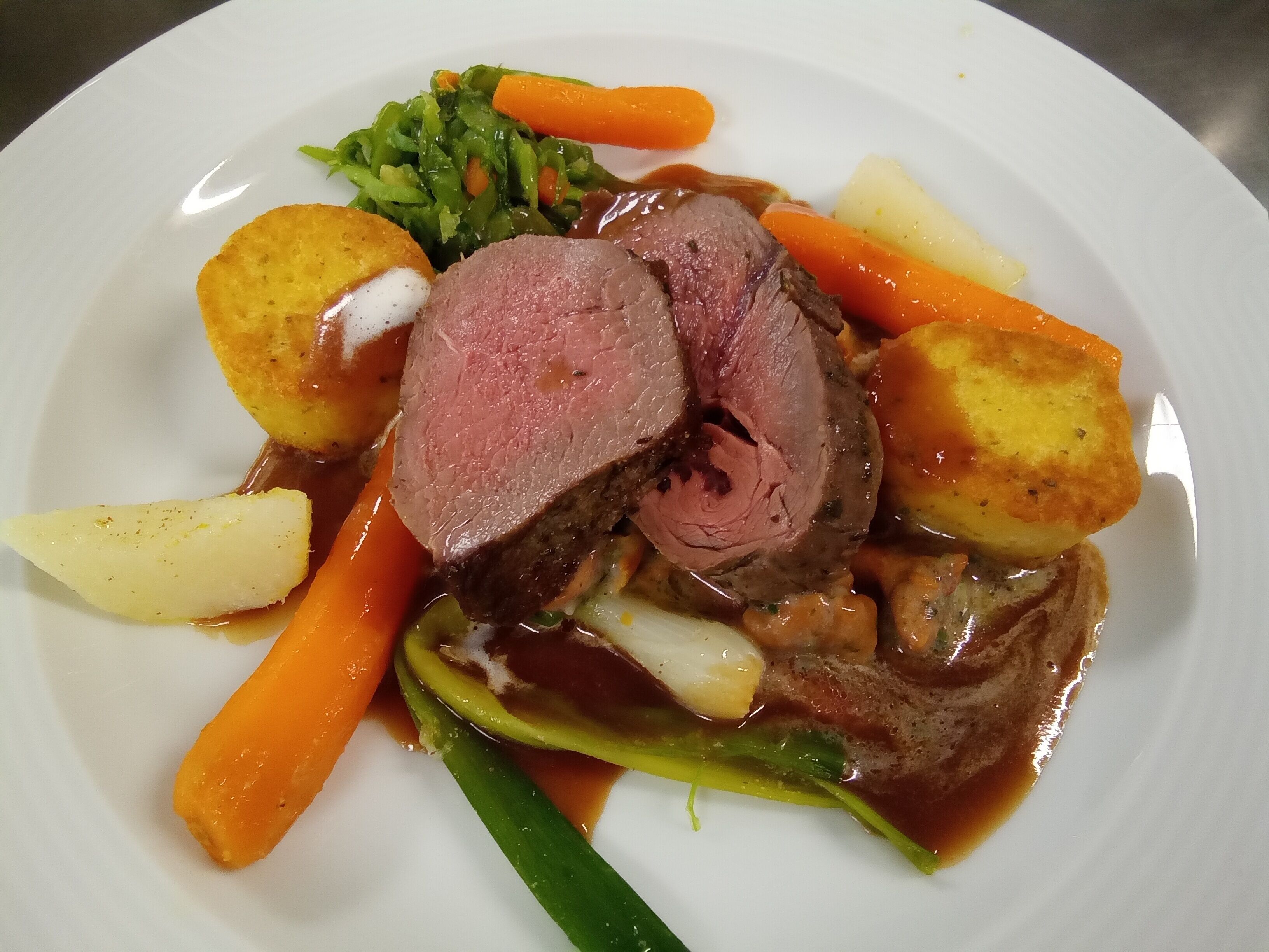 A plate of food with roast beef, carrots, potatoes, and green vegetables.