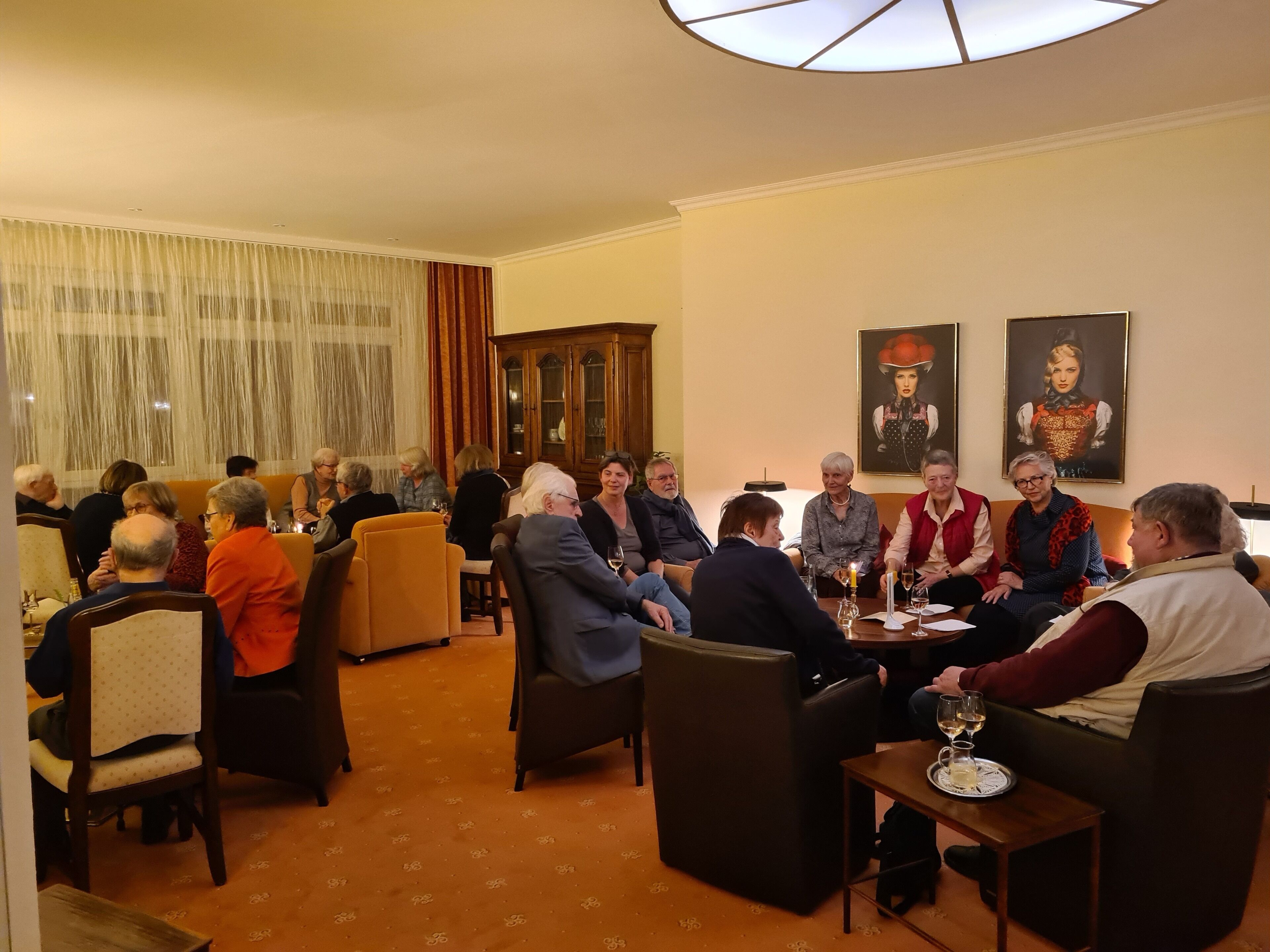 Ein formeller Speisesaal mit runden Tischen und Stühlen, einer großen Holzvitrine und zwei gerahmten Portraits an der Wand.