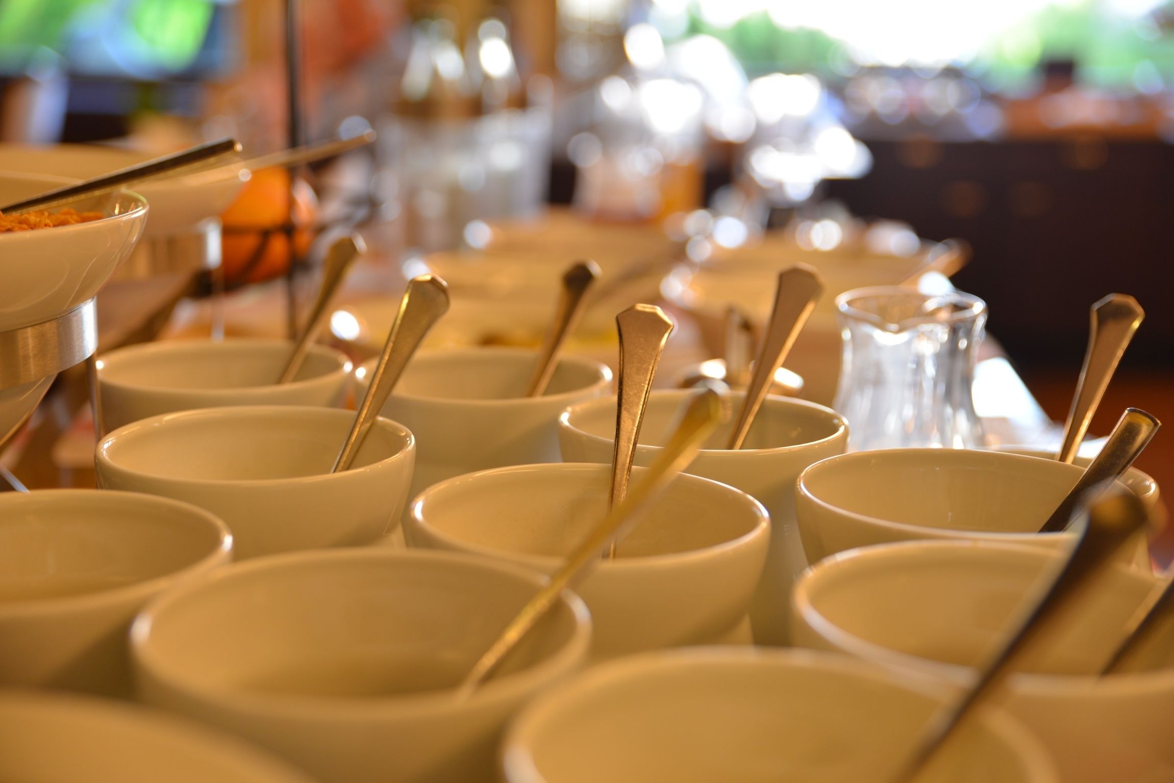 A row of white bowls with spoons, arranged on a table.