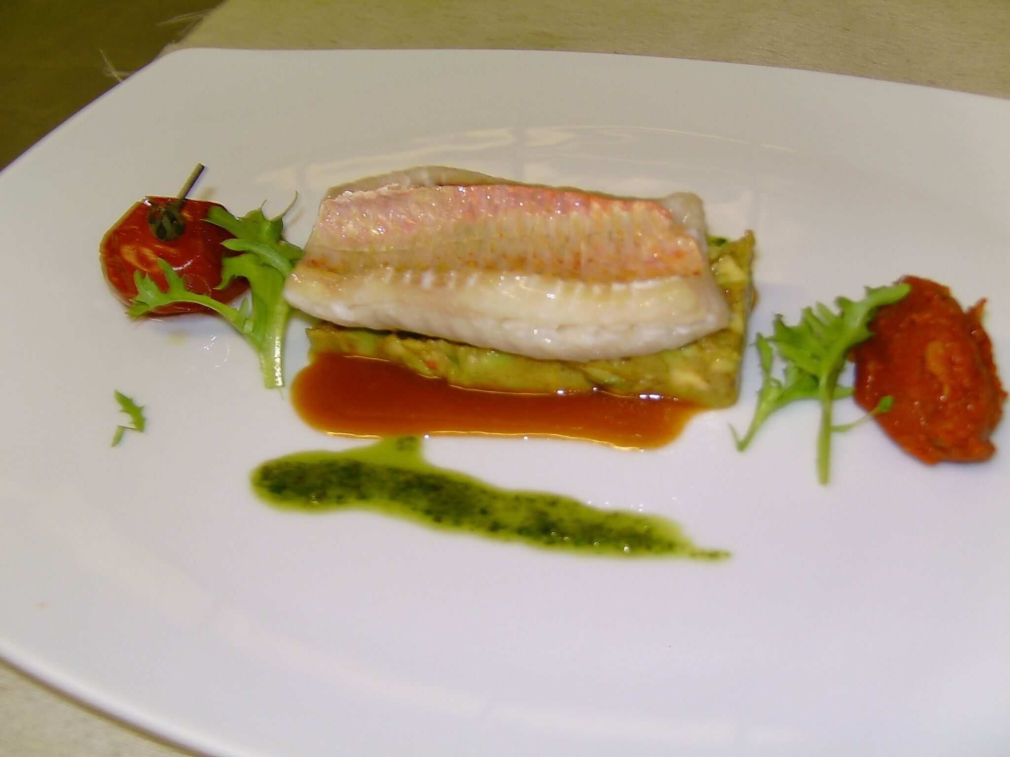 Un plato blanco con un trozo de pescado, aguacate y salsa.