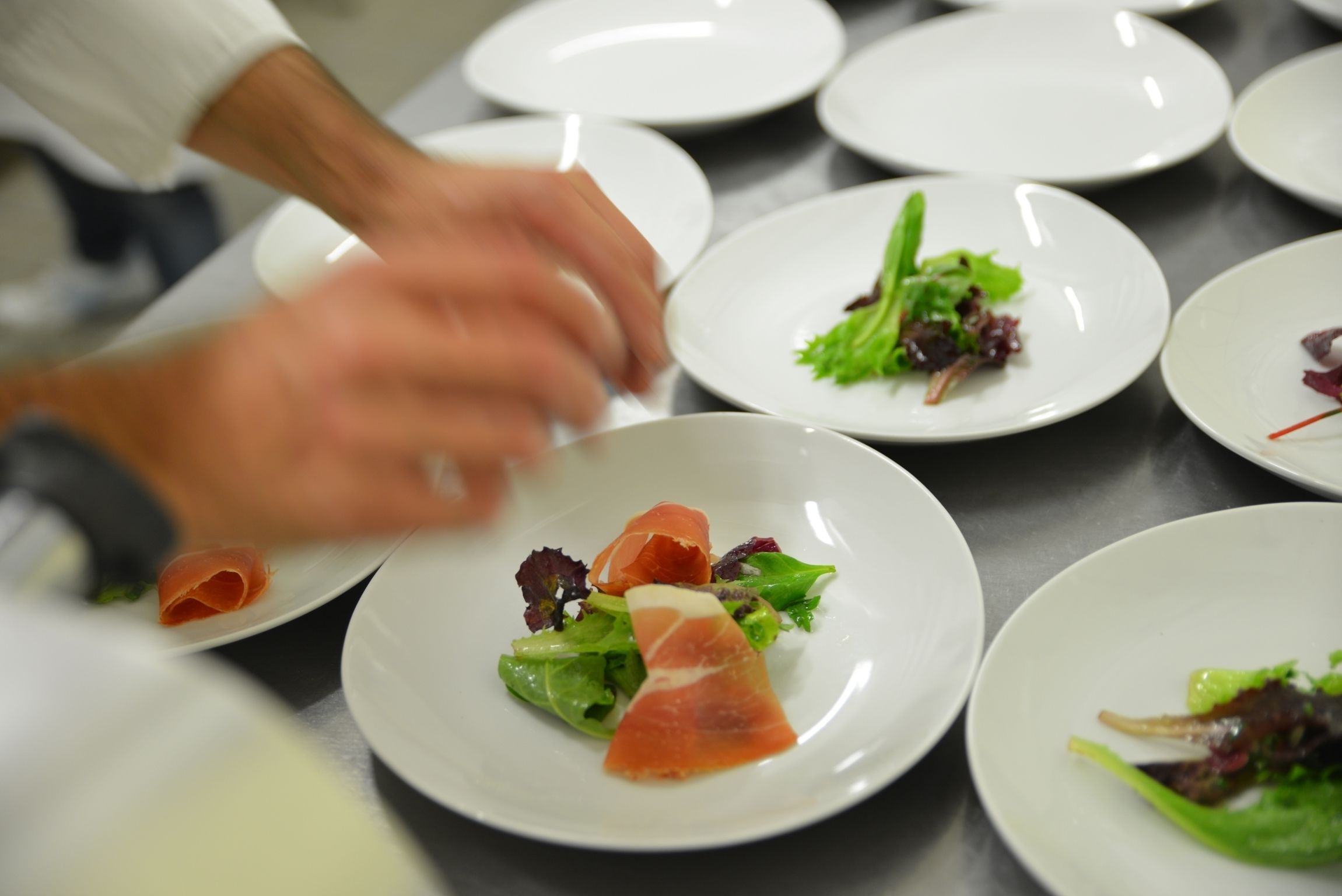 Un chef preparando platos sobre una mesa de acero inoxidable con platos blancos.