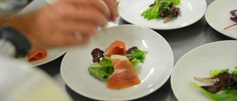 A chef preparing dishes on a stainless steel table with white plates.