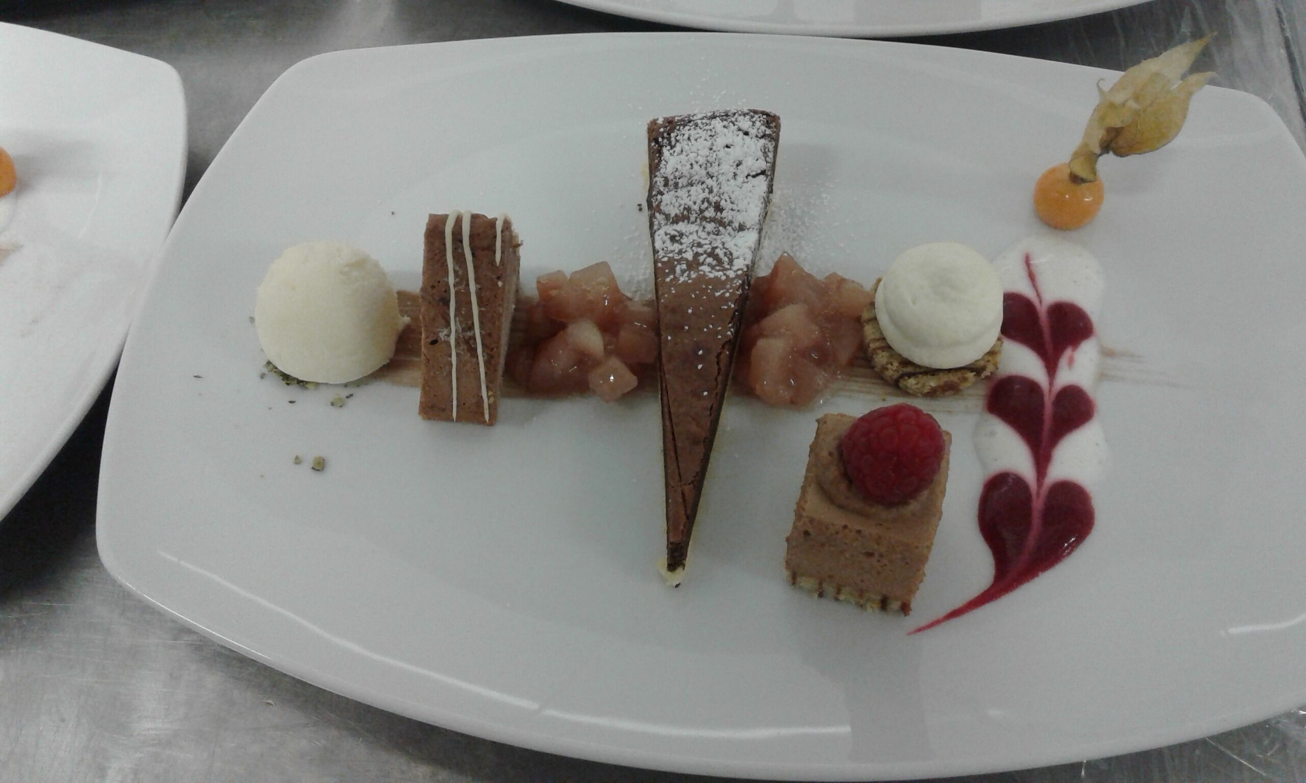 Een taartbord met diverse lekkernijen, waaronder een stuk chocolade, een framboos en een witte bol.
