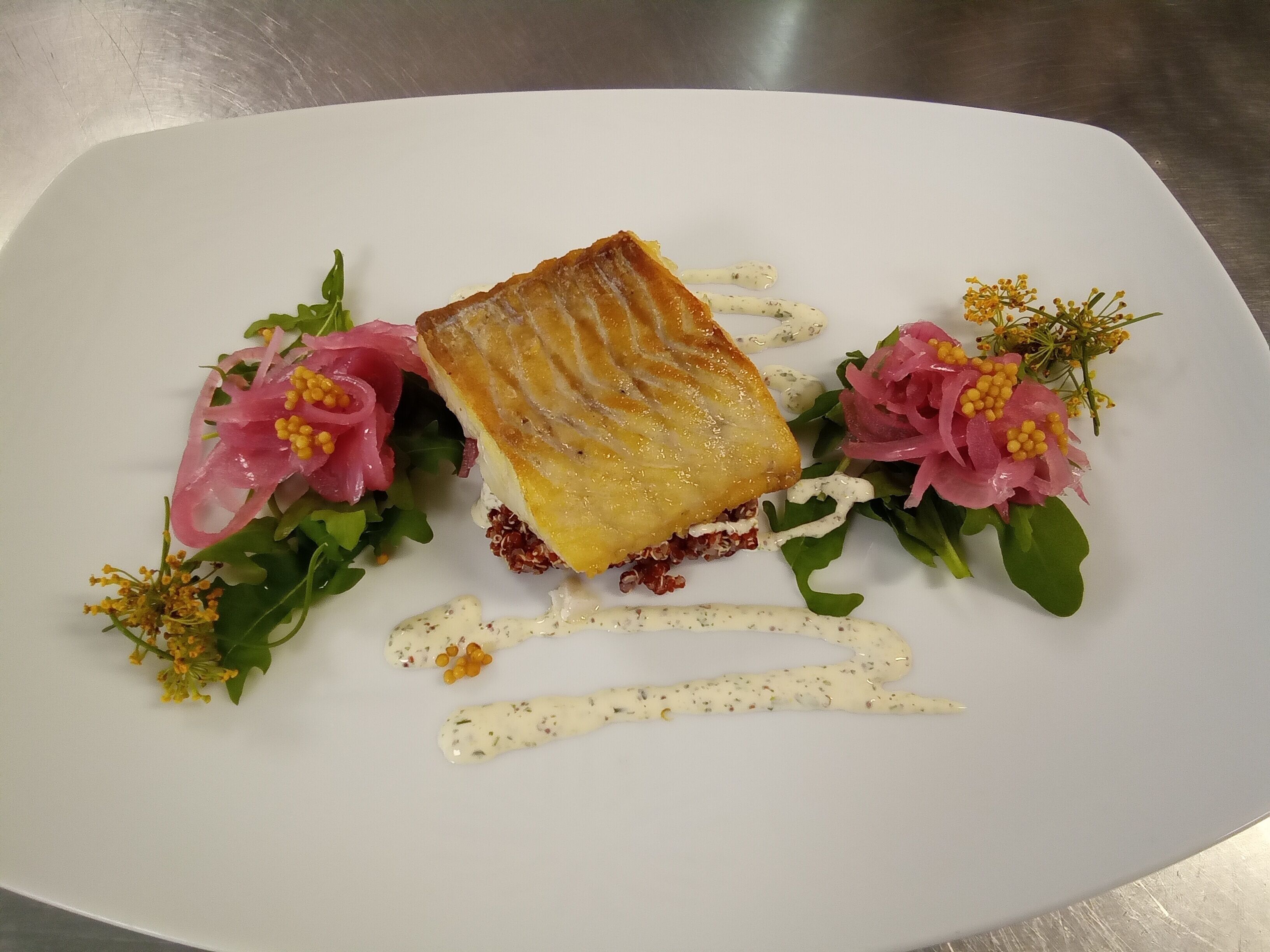 A white plate with a piece of food, possibly a pastry, surrounded by greens and pink flowers.