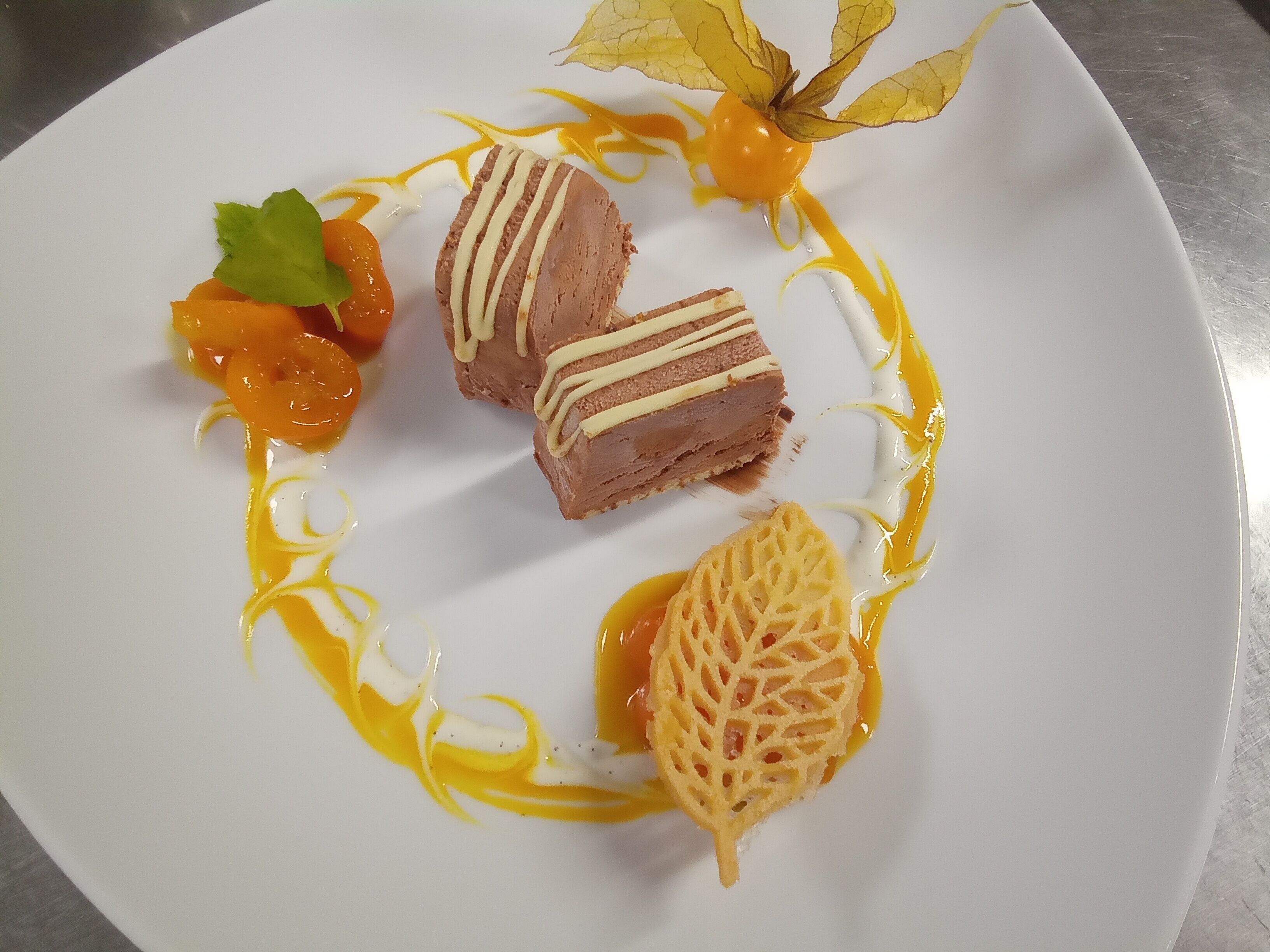 Une assiette à dessert contenant divers éléments, notamment une part de gâteau recouverte de glaçage blanc, une garniture de fruits et une feuille décorative.