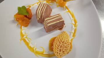 Une assiette à dessert contenant divers éléments, notamment une part de gâteau recouverte de glaçage blanc, une garniture de fruits et une feuille décorative.