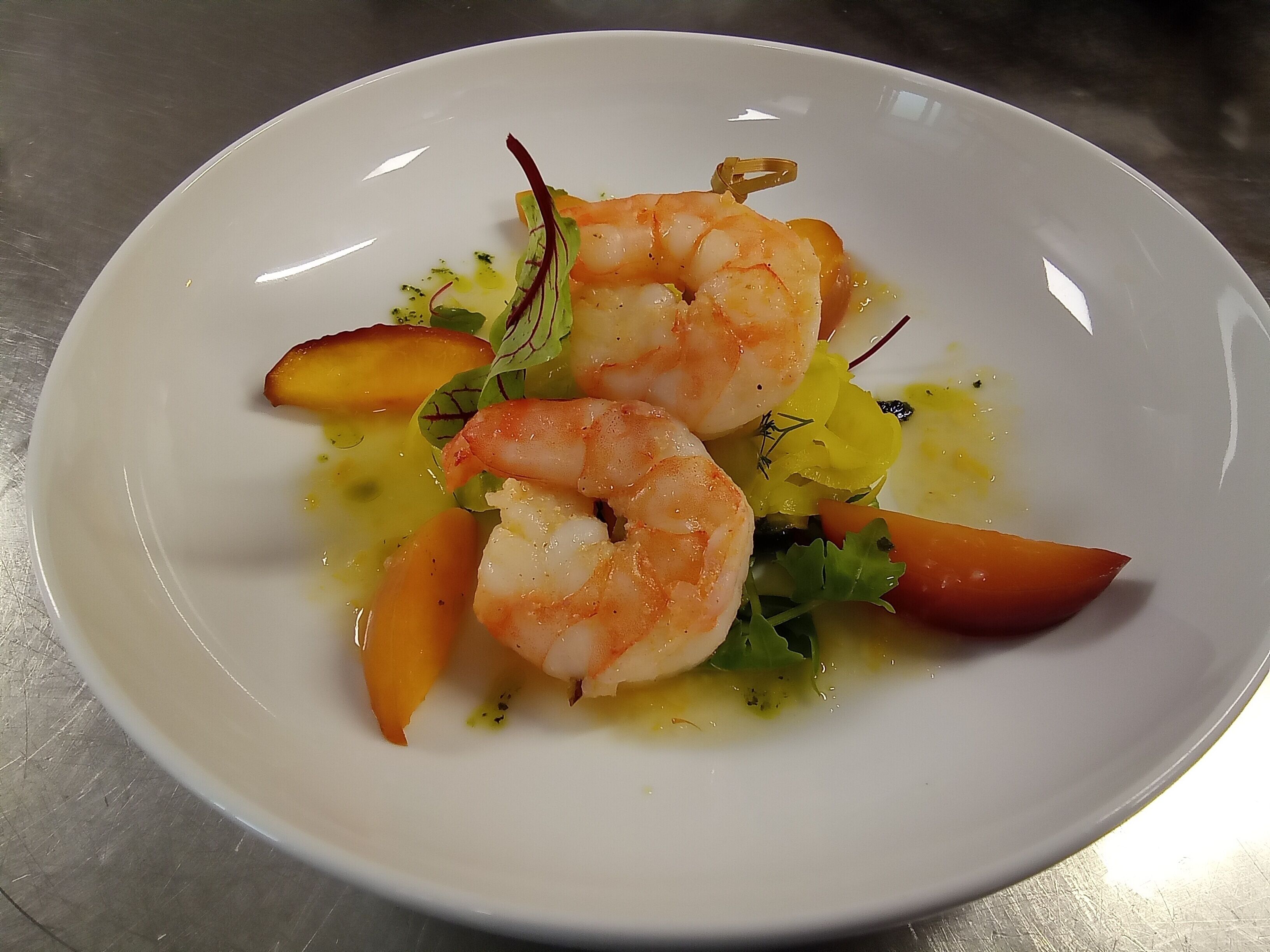 A white plate with three shrimp, some greens, and slices of peach.