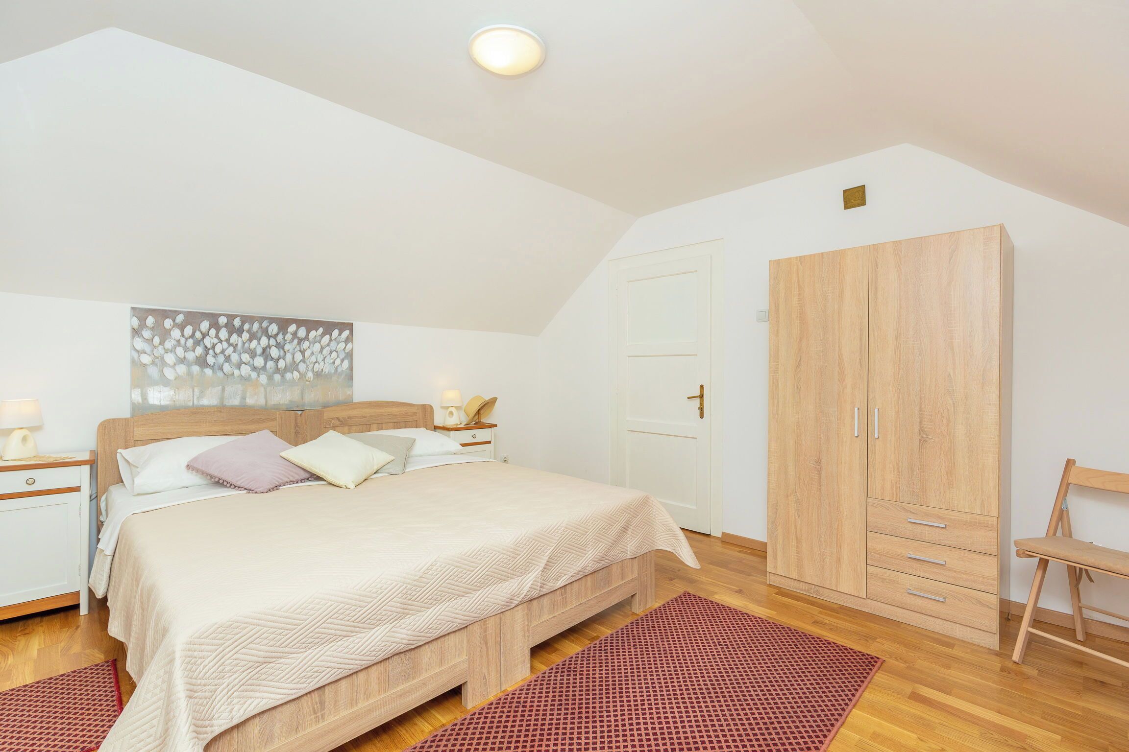 A bedroom with a bed, wooden wardrobe, and a red patterned rug.
