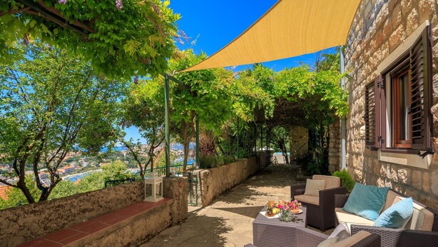 A patio with wicker furniture, a stone wall, and a view of the city. - Villa Isanda - Four Bedroom Villa, Sleeps 8 (Dubrovnik)