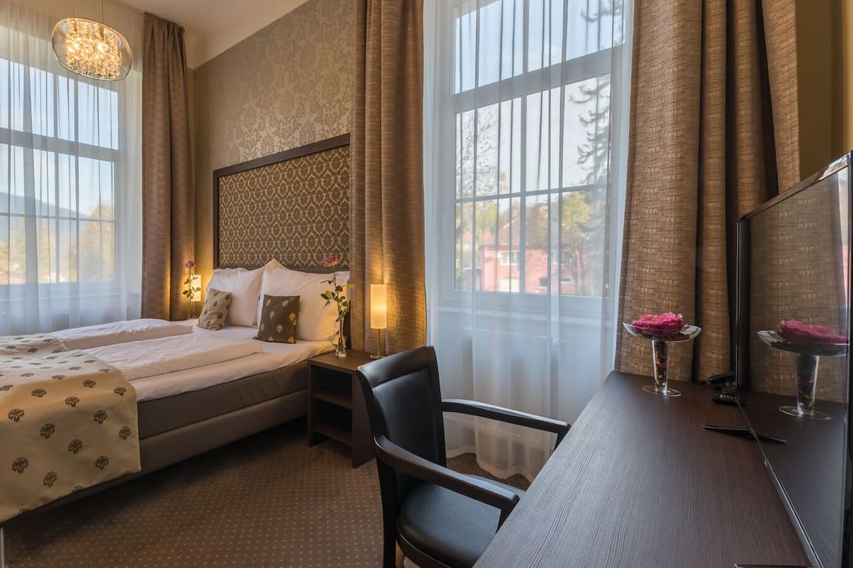 Ein Hotelzimmer mit einem großen Bett, einem Schreibtisch und zwei mit Vorhängen versehenen Fenstern.